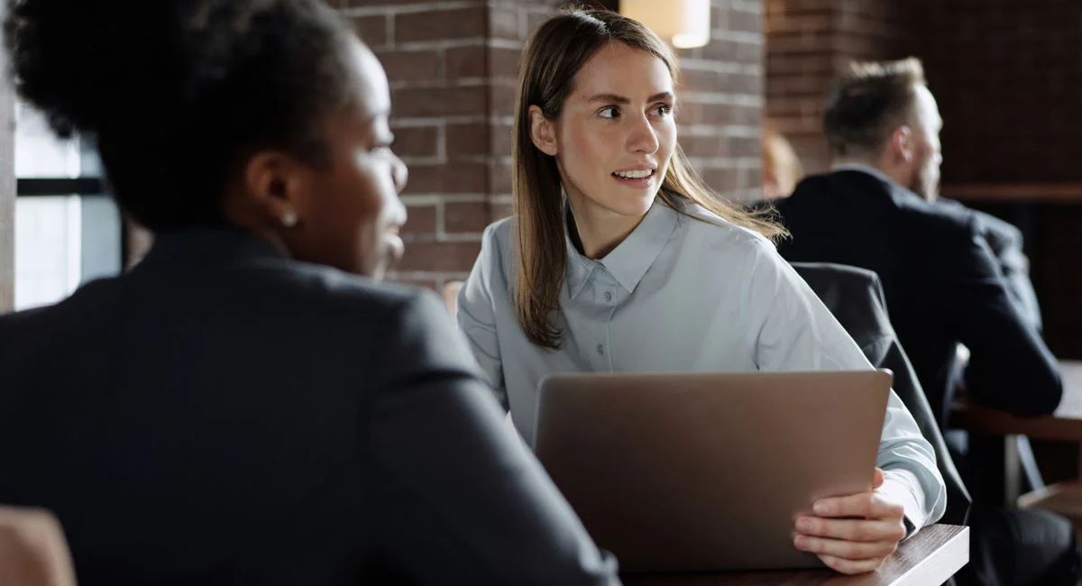 Business professionals engaged in conversation at a modern café with laptops.