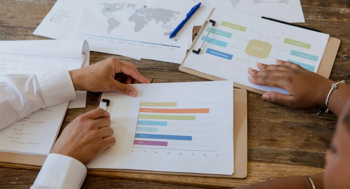 Top view of colleagues discussing charts and graphs on a wooden table during a business meeting.