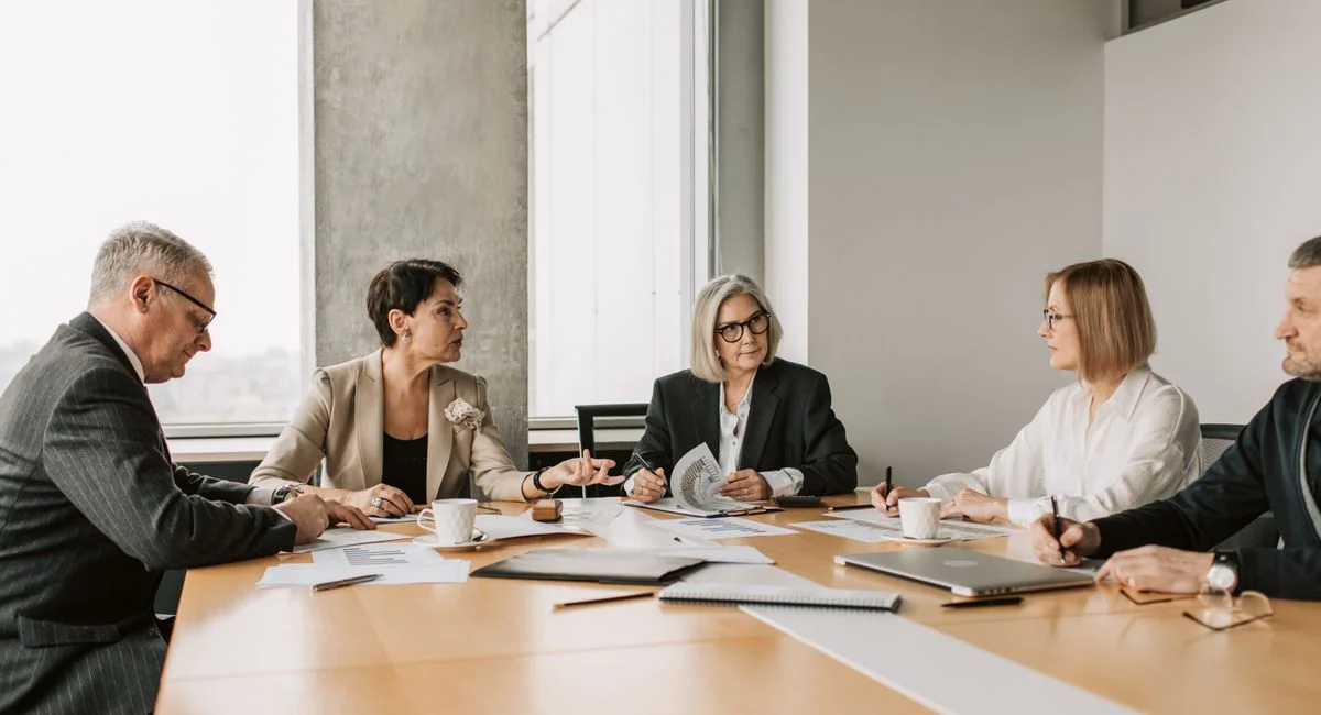 Five business professionals engaged in a meeting in a modern office setting, discussing documents and ideas.