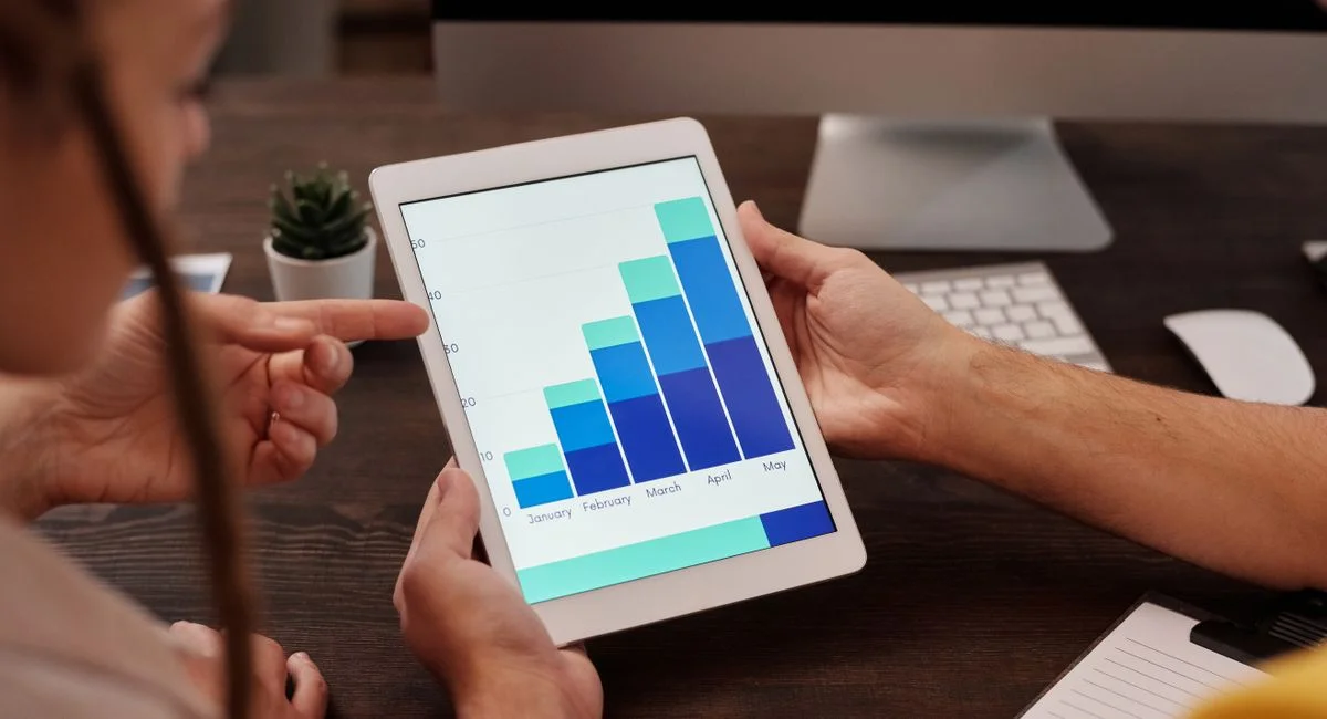 Two adults working in an office, examining graphs on a tablet screen for data analysis.